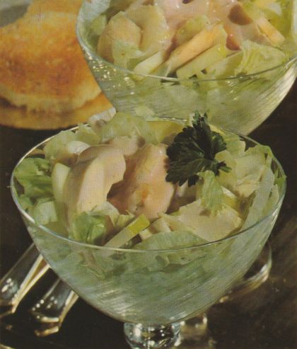 Cocktailschalen mit geschichtetem Geflügelsalat auf Salatblättern, garniert mit Petersilie. Im Hintergrund weitere gefüllte Glasschalen mit Hähnchen–Staudensellerie–Salat und Weißbrotscheiben auf einem Teller.