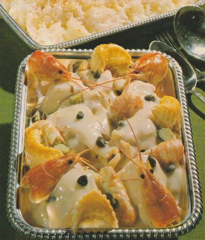 Hühnerfrikassee in cremiger Sauce mit Kapern, garniert mit ganzen Flusskrebsen und Blätterteig-Fleurons in einer silbernen Servierform. Im Hintergrund eine Auflaufform mit Reis auf einer Textilserviette.