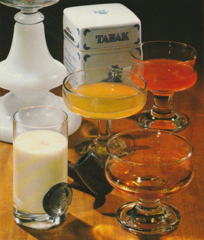 Vier Cocktails in verschiedenen Gläsern: ein cremiger Rum–Egg–Nogg in einem Tumbler, ein Mañana in einer Cocktailschale, ein weiterer Cocktail in einer Sektschale und ein Rum–Cocktail in einer flachen Schale. Im Hintergrund ein weißer Kerzenständer und eine Tabakdose aus Porzellan. Die Getränke zeigen unterschiedliche Konsistenzen von milchig bis klar.