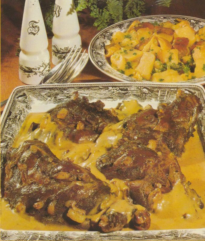 Gebratene Hasenkeulen in einer silbernen Servierplatte mit glänzender Sauce, dahinter ein Teller mit Salzkartoffeln und Steinpilzen, im Hintergrund Salzstreuer und Gabel auf hölzernem Untergrund