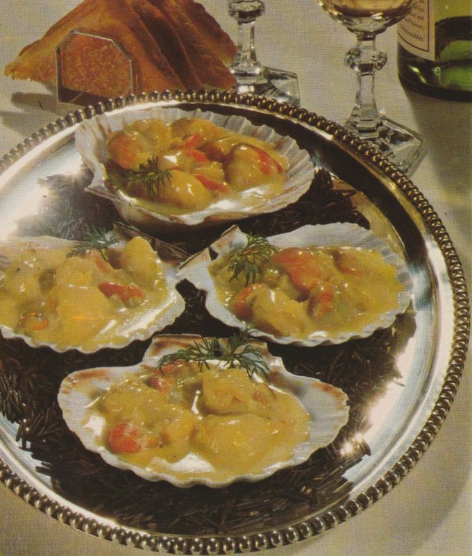 Vier geöffnete Jakobsmuscheln in ihren Schalen liegen auf einem silbernen Tablett, serviert in einer cremigen gelben Sauce mit Garnelen und frischem Dill garniert. Im Hintergrund sind Kristallgläser und getoastetes Brot zu sehen.