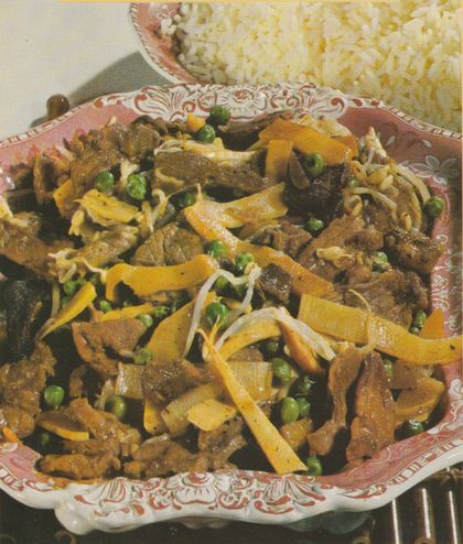 Gebratene Schweinefleisch-Streifen mit gelben Bambussprossen-Streifen, grünen Erbsen, Sojakeimen und chinesischen Pilzen in einer Sojasauce, serviert auf einer rot-weiß gemusterten Platte im Retro-Stil. Im Hintergrund eine Portion locker gekochter Reis.