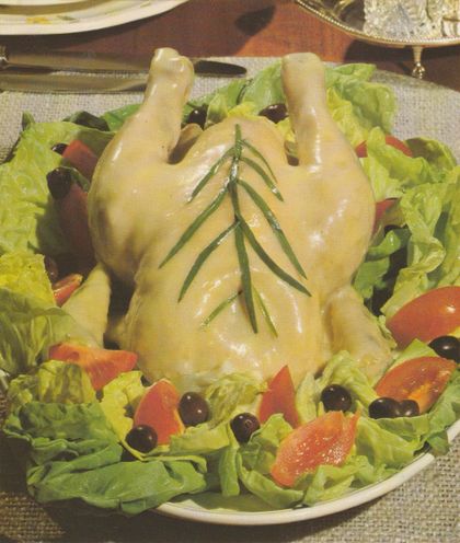 Pochierte Poularde auf einem Bett aus Kopfsalat, garniert mit Tomatenschnitzen und schwarzen Oliven. Das Geflügel ist mit einer hellen Sauce überzogen und mit Estragonblättern dekoriert. Im Hintergrund sind weitere Teller auf einem gedeckten Tisch zu sehen.