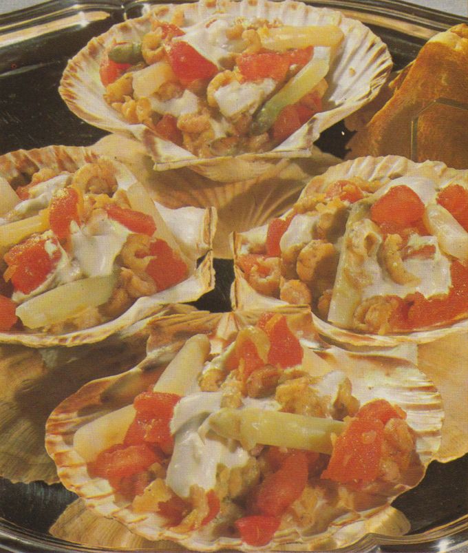 Vier geöffnete Jakobsmuscheln in ihrer gerillten Schale, gefüllt mit Muschelfleisch, leuchtend orangen Rogen, Gemüsestückchen und einer hellen Sauce. Die Muscheln sind kreisförmig arrangiert.