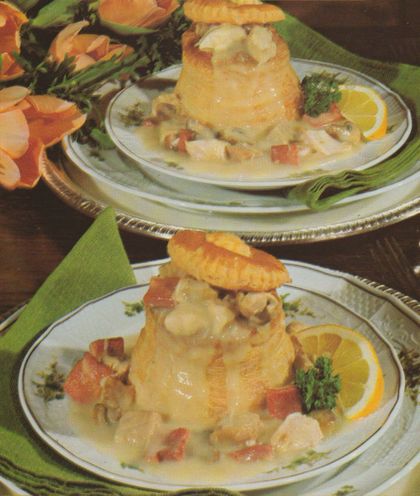 Blätterteigpasteten gefüllt mit Ragout aus Hähnchen, Kalbfleisch, Champignons und Rinderzunge in heller Sauce, angerichtet auf Tellern mit Zitronenspalten und Petersilie als Garnitur, im Hintergrund Schnittblumen als Tischdekoration