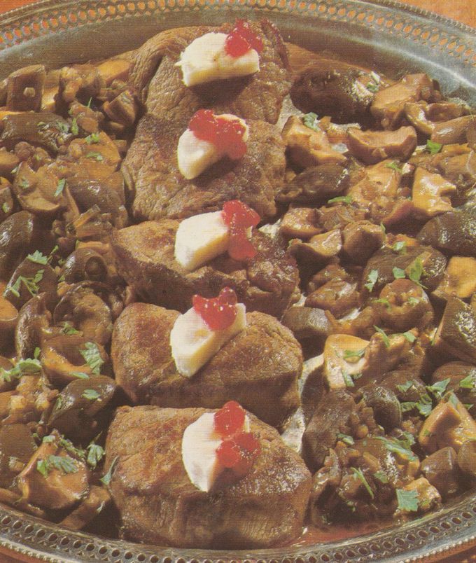 Gebratene Hirschnüßchen auf einer Platte, jeweils garniert mit einer Bananenscheibe und einem Klecks Preiselbeeren, umgeben von gebratenen Waldpilzen mit Petersilie bestreut.