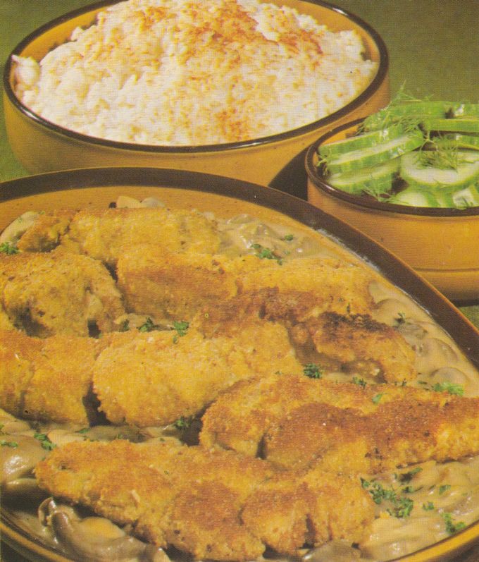 Gebratene, goldbraun panierte Kalbsbries-Scheiben auf cremigen Champignons in heller Sauce, dazu eine große Schüssel Reis und ein Gurkensalat in braunen Schalen auf einer Holzunterlage.