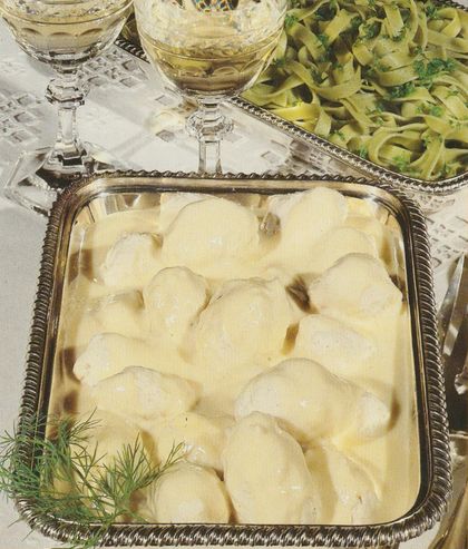Hechtklößle in cremiger Sauce auf einem silbernen Tablett mit verziertem Rand, daneben Weingläser mit Weißwein, eine Schale mit Nudeln und frischer Dill als Garnitur.
