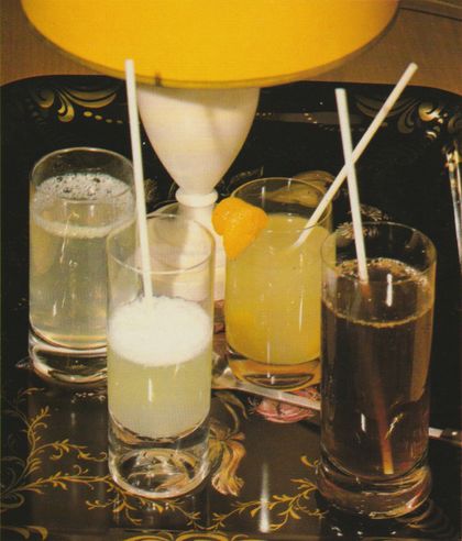 Vier verschiedene Getränke mit weißen Strohhalmen stehen auf zwei schwarzen Tabletts mit goldenem Blumenmuster, dahinter eine gelbe Schüssel.