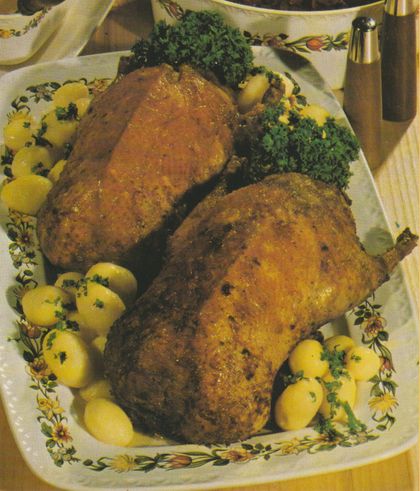 Zwei goldbraun gebratene Wildenten auf einer ovalen Servierplatte mit Blumenmuster, umgeben von petersilienbestreuten Salzkartoffeln und Petersilie als Garnitur.