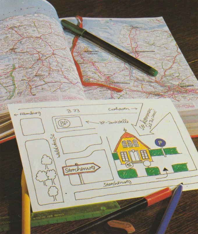 Eine handgezeichnete Wegbeschreibung zeigt den Weg von Hamburg über Cuxhaven zu einem gelben Haus, darüber liegt eine Straßenkarte von Norddeutschland. Mehrere Buntstifte liegen auf der Karte und der Wegskizze verteilt.