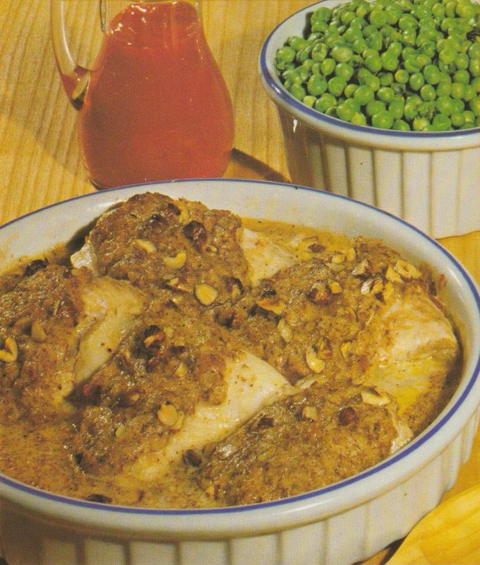 Fischfilets in einer Auflaufform mit Haselnuss–Käse–Kruste, goldbraun überbacken. Im Hintergrund eine Schüssel mit Erbsen und eine Karaffe mit Tomatenketchup.